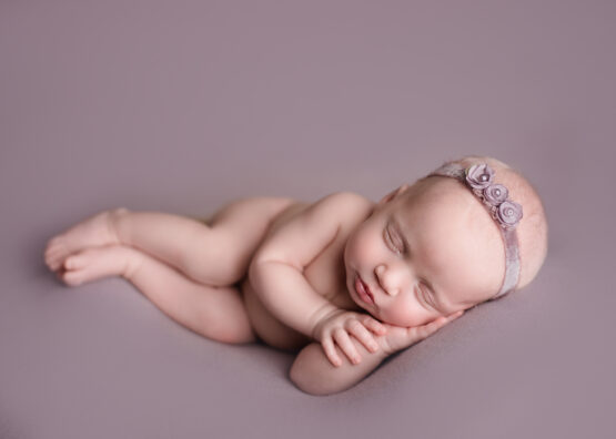 Michigan newborn photographer Melissa Anne Photography baby girl sidelay pose with dusty purple backdrop and flower headband