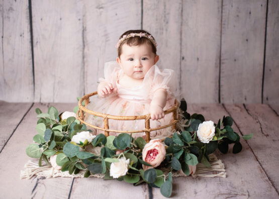 Metro Detroit photographer Melissa Anne Photography sitter photo session with six month old girl in bamboo basket with flowers on wood backdrop