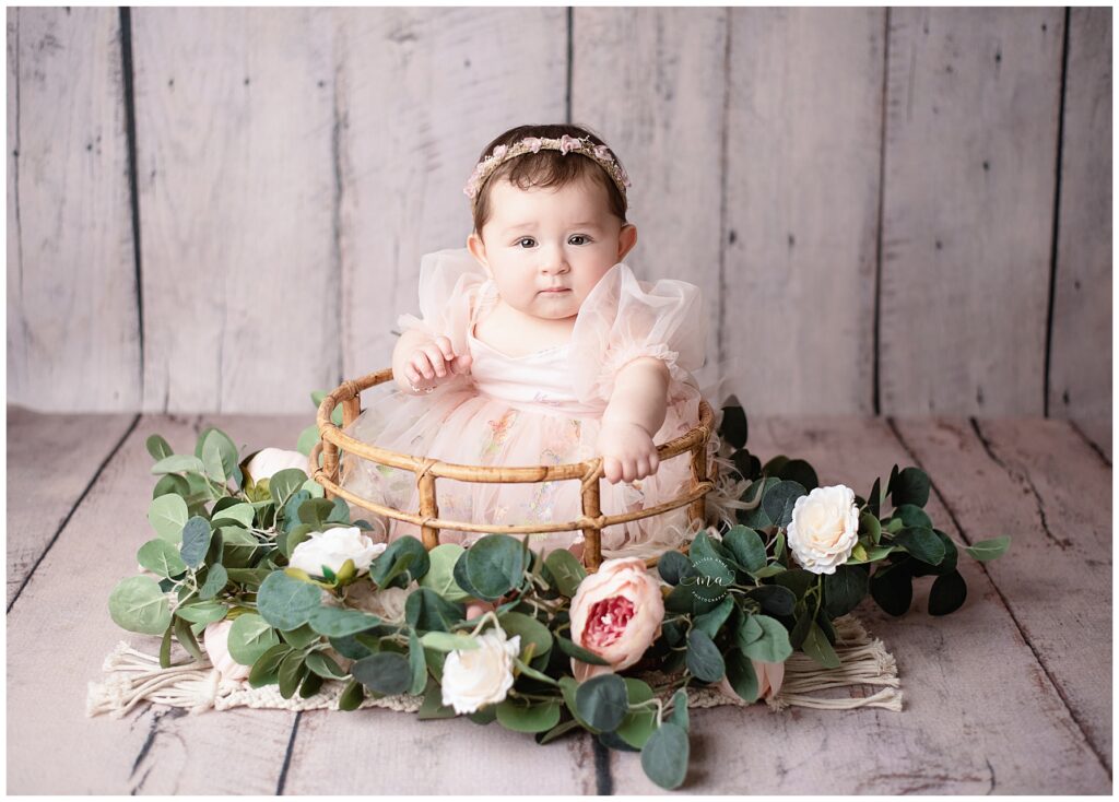 Metro Detroit photographer Melissa Anne Photography sitter photo session with six month old girl in bamboo basket with flowers on wood backdrop
