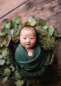 posed-newborn-photography-Troy Michigan newborn photographer Melissa Anne Photography baby boy in green wrap in bucket with eyes open