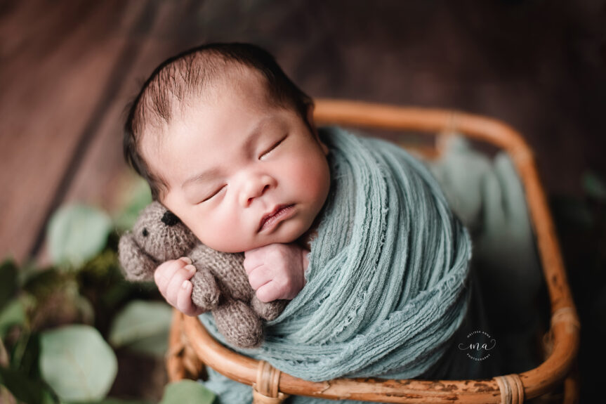Troy Michigan newborn photographer Melissa Anne Photography baby boy with dark hair wrapped in sage green wrap holding teddy bear