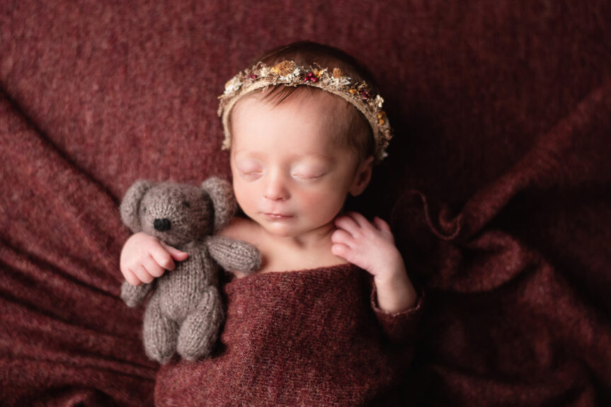 Troy Michigan newborn photographer Melissa Anne Photography cute newborn photo of girl holding bear dark burgundy backdrop floral headband