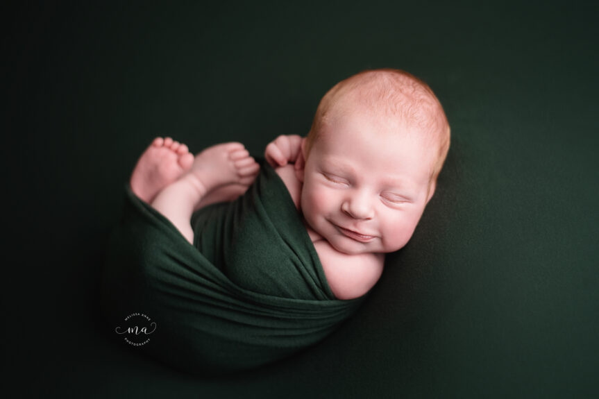 Troy Michigan newborn photographer Melissa Anne Photography newborn baby boy wrapped in dark green smiling