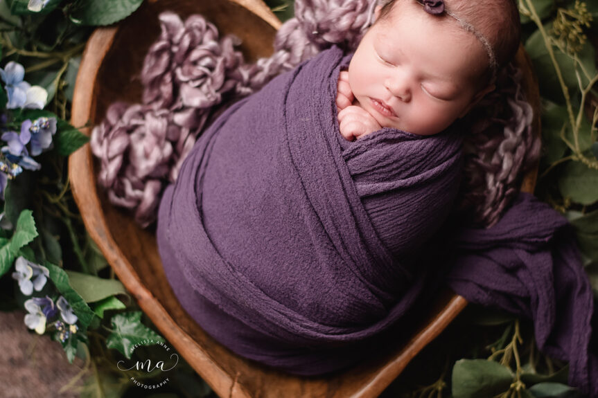 Utica Michigan newborn photographer Melissa Anne Photography baby girl wrapped in purple in wood heart bowl with flowers