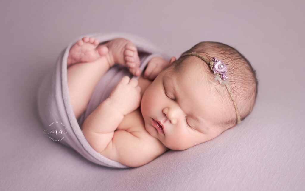 newborn baby girl swaddled in light purple wrap with floral headband in Metro Detroit Photographer Melissa Anne Photography studio